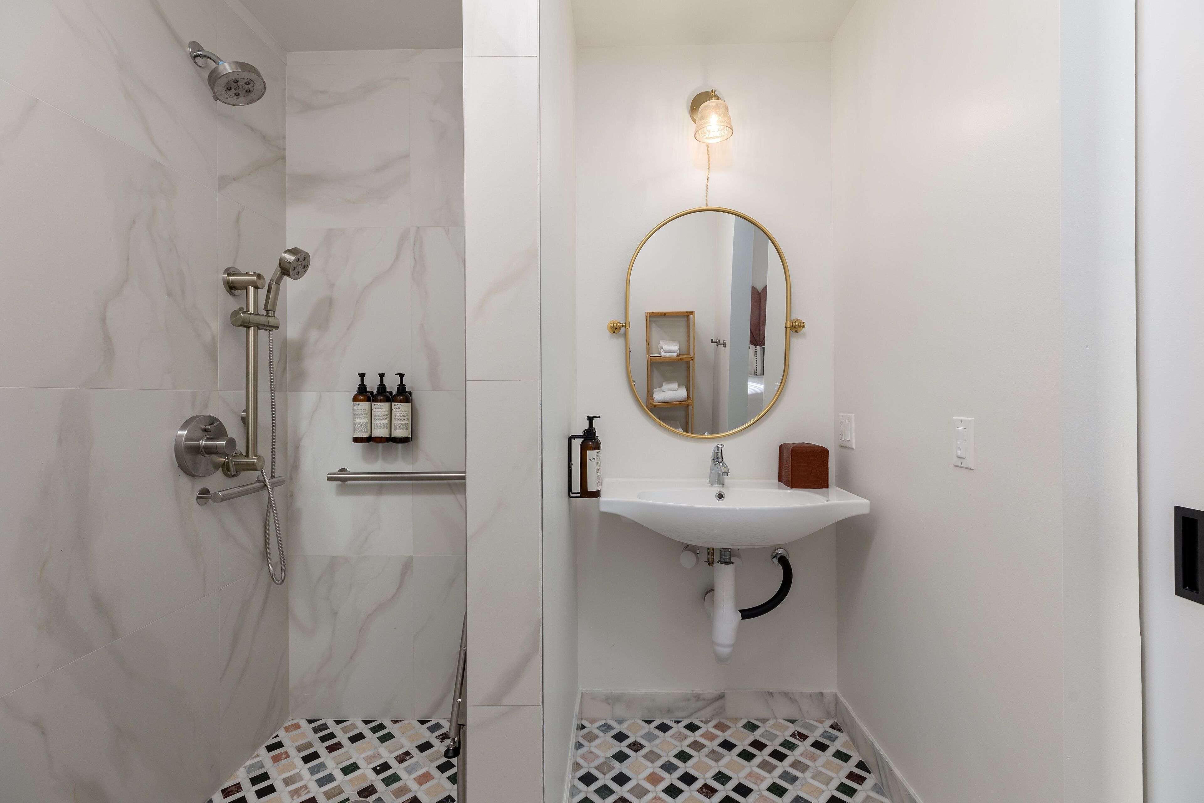 A bathroom with a shower, a sink, a mirror, and toiletries on a shelf.