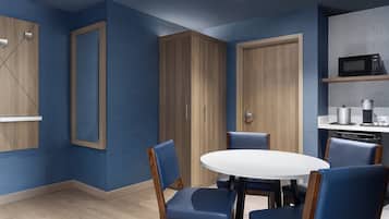A modern kitchen with a white round table and blue chairs, wooden cabinets, and a microwave on the countertop.