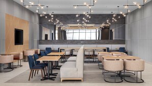 A modern conference room with multiple tables and chairs, a large sofa, and a television on the wall. - Holiday Inn Express Montreal Airport - St-Laurent by IHG (Montreal)