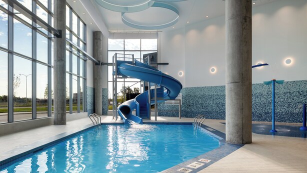 An indoor swimming pool with a blue slide, large windows, and a modern ceiling design. - Holiday Inn Express Montreal Airport - St-Laurent by IHG (Montreal)
