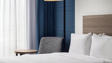 A hotel room with a bed, a small round table, a chair, and a lamp.