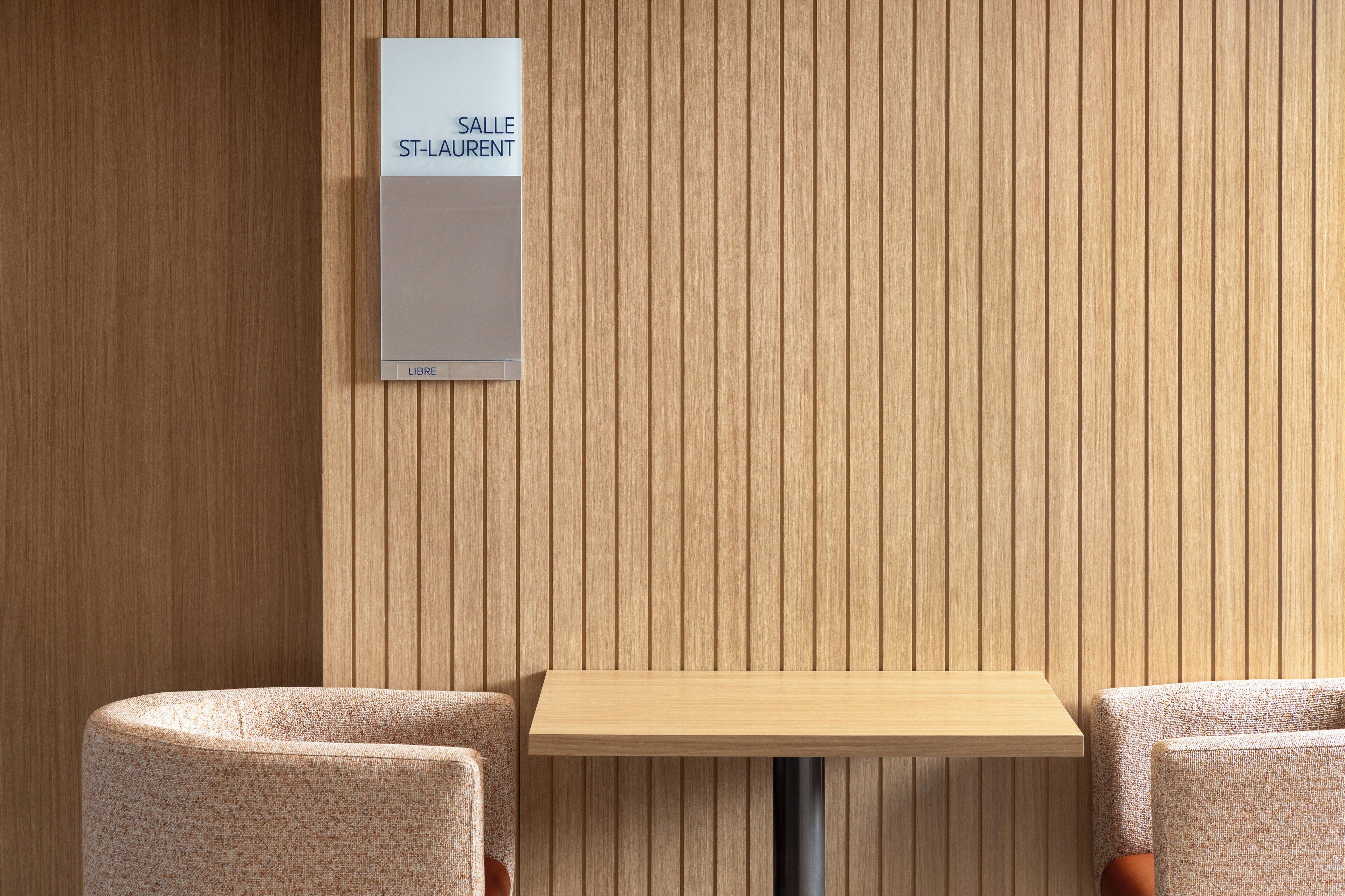 A room with a wooden panel wall, a sign reading 'ST-LAURENT', and a small table with two chairs.