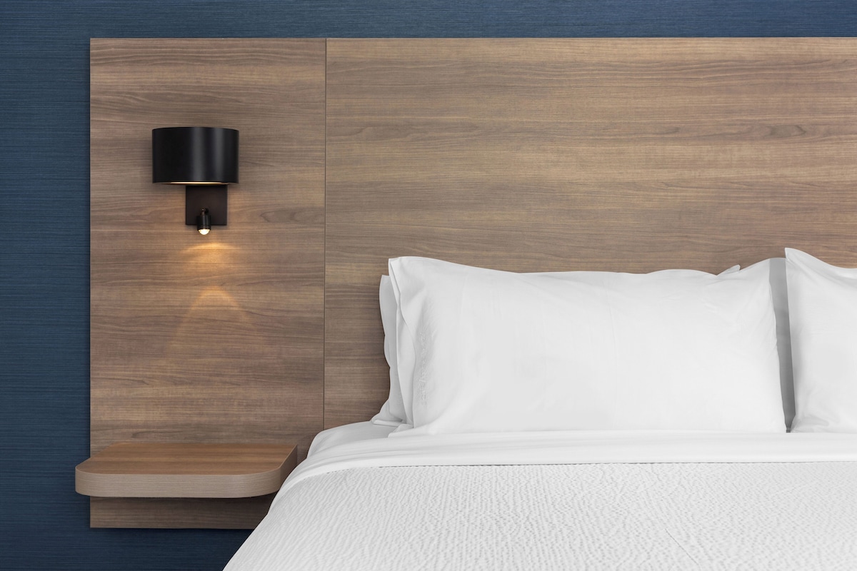 Un dormitorio con cabecera de madera, ropa de cama blanca y lámpara fijada a la pared.