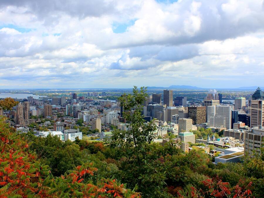 A cityscape with a mix of modern and older buildings, a river in the background, and a view of distant mountains.
