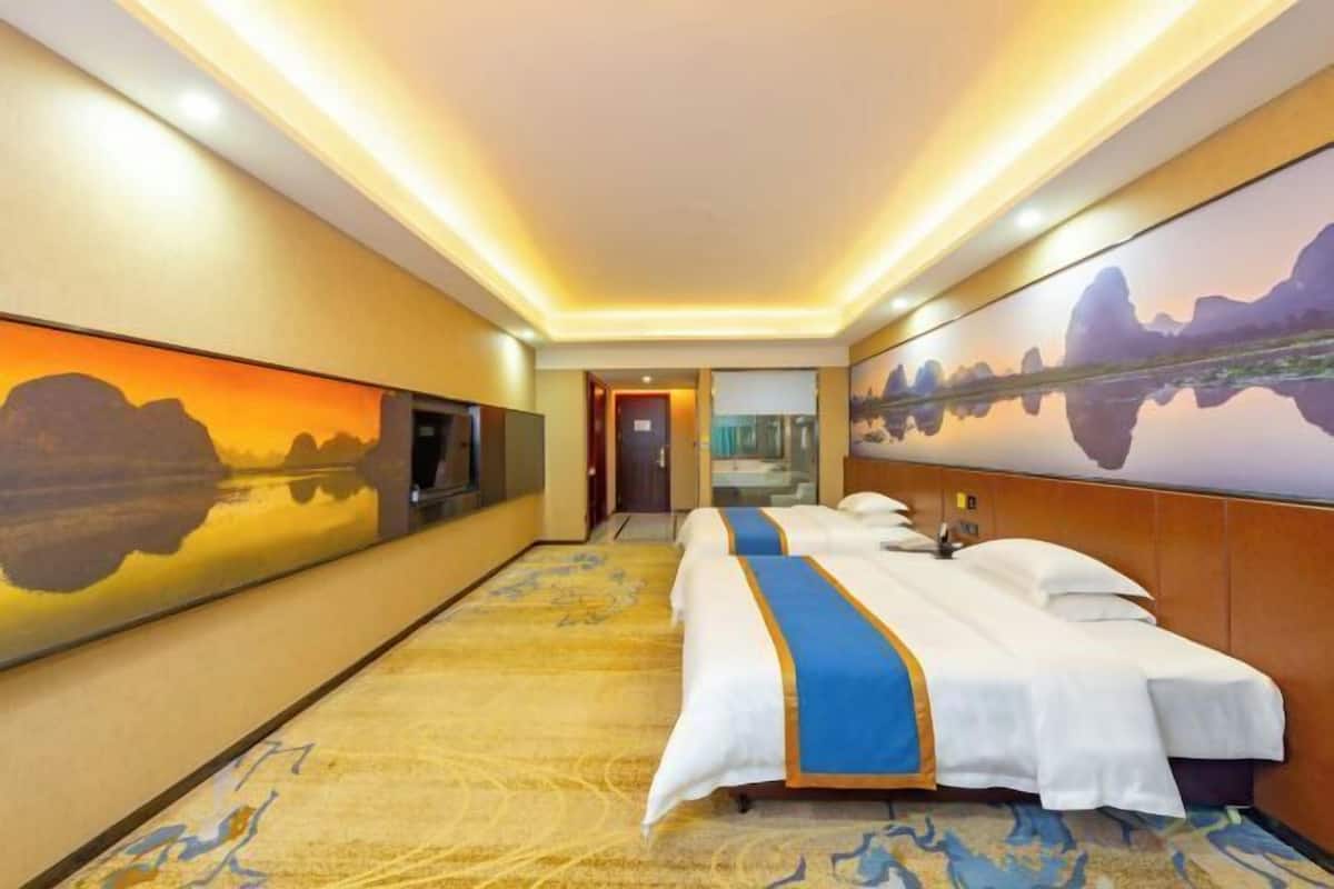 A hotel room with a bed, a TV, and a large painting on the wall.