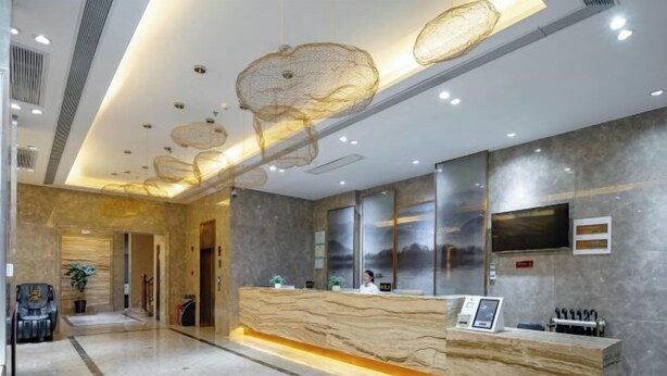 A modern reception area with a marble reception desk, a mounted television, and a seating area with a chair and a plant. - Manhattan Hotel Guilin Liangjiang Sihu Arctic Plaza (Guilin)