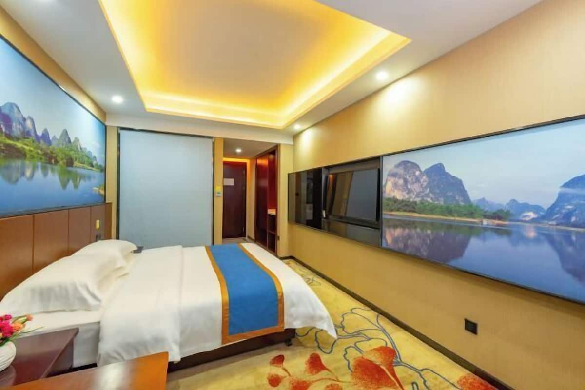 A hotel room with a bed, a desk, a chair, a TV, and a large window with a mountain view.