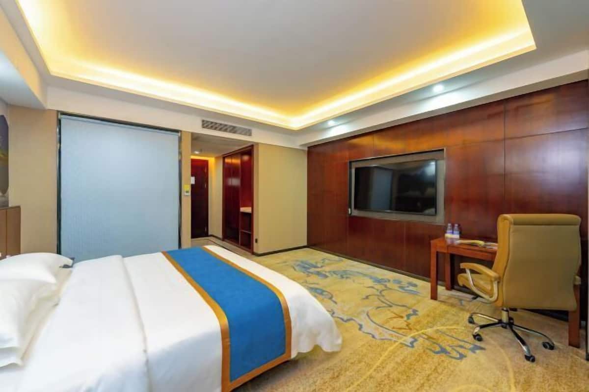A hotel room with a bed, a desk, a chair, a television, and a carpeted floor.