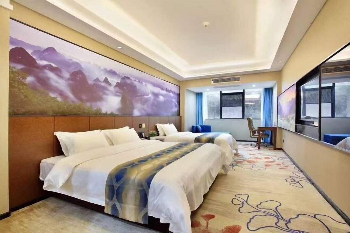 A hotel room with two beds, a large wall-mounted TV, and a carpeted floor.