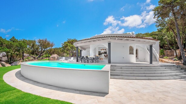 Una villa moderna con piscina, mobiliario exterior y un patio cubierto.