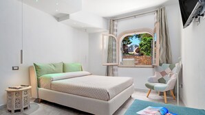 Un dormitorio moderno con cama, mesita de noche, silla, ventana con cortinas y televisor de pantalla plana montado en la pared.