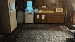 Una cucina compatta con mobili in legno, un frigorifero, un fornello, un forno a microonde e una finestra con tende.