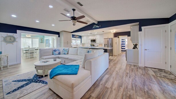 A spacious living room with a large L-shaped sofa, a dining area with white furniture, and a kitchen with white cabinets and stainless steel appliances. - 3-BR/2 Bath waterfront home with direct access to Gulf. Pool, kayaks and dock (Hernando Beach)