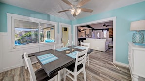 A dining area with a dark wooden table, white chairs, and blue-striped placemats. There is a ceiling fan above and a view of a kitchen and living area through an open door. - 3-BR/2 Bath waterfront home with direct access to Gulf. Pool, kayaks and dock (Hernando Beach)