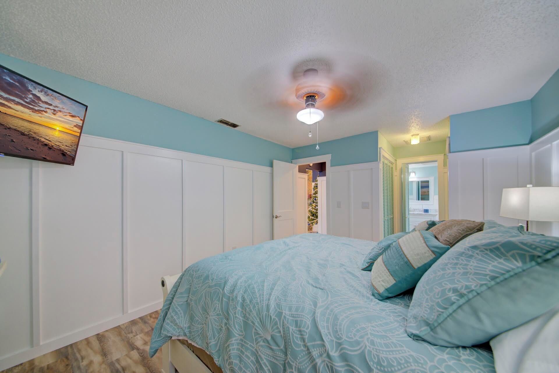 A bedroom with a bed, a ceiling fan, and a wall-mounted TV.