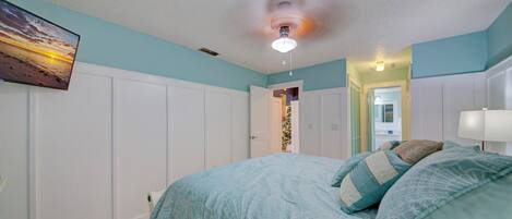 A bedroom with a bed, a ceiling fan, and a wall-mounted TV.