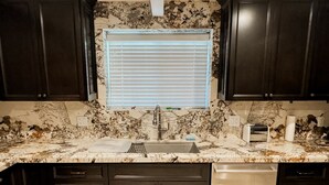 Una cocina con armarios oscuros, encimera de mármol, un lavabo y una ventana con persianas.