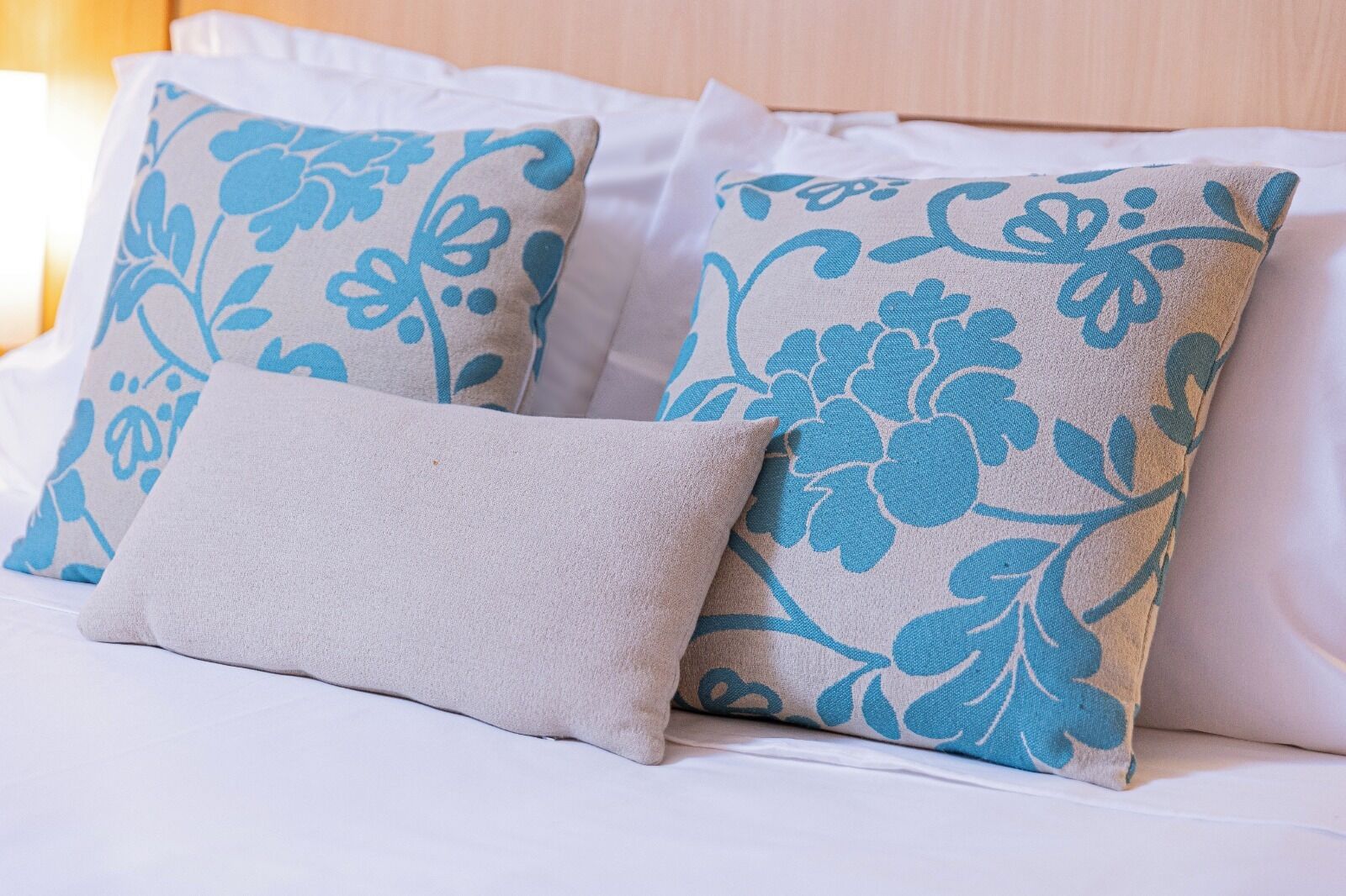 A bed with white bedding and decorative pillows with blue floral patterns.