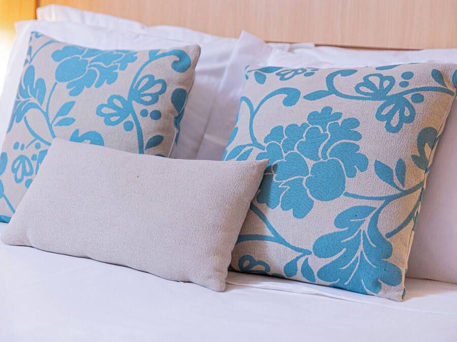 A bed with white bedding and decorative pillows with blue floral patterns.