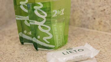 A bathroom countertop with a green bottle of shampoo, a green bottle of conditioner, and a packet of body wash.