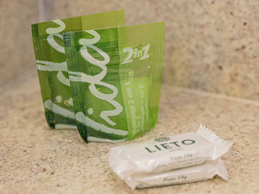 A bathroom countertop with a green bottle of shampoo, a green bottle of conditioner, and a packet of body wash.
