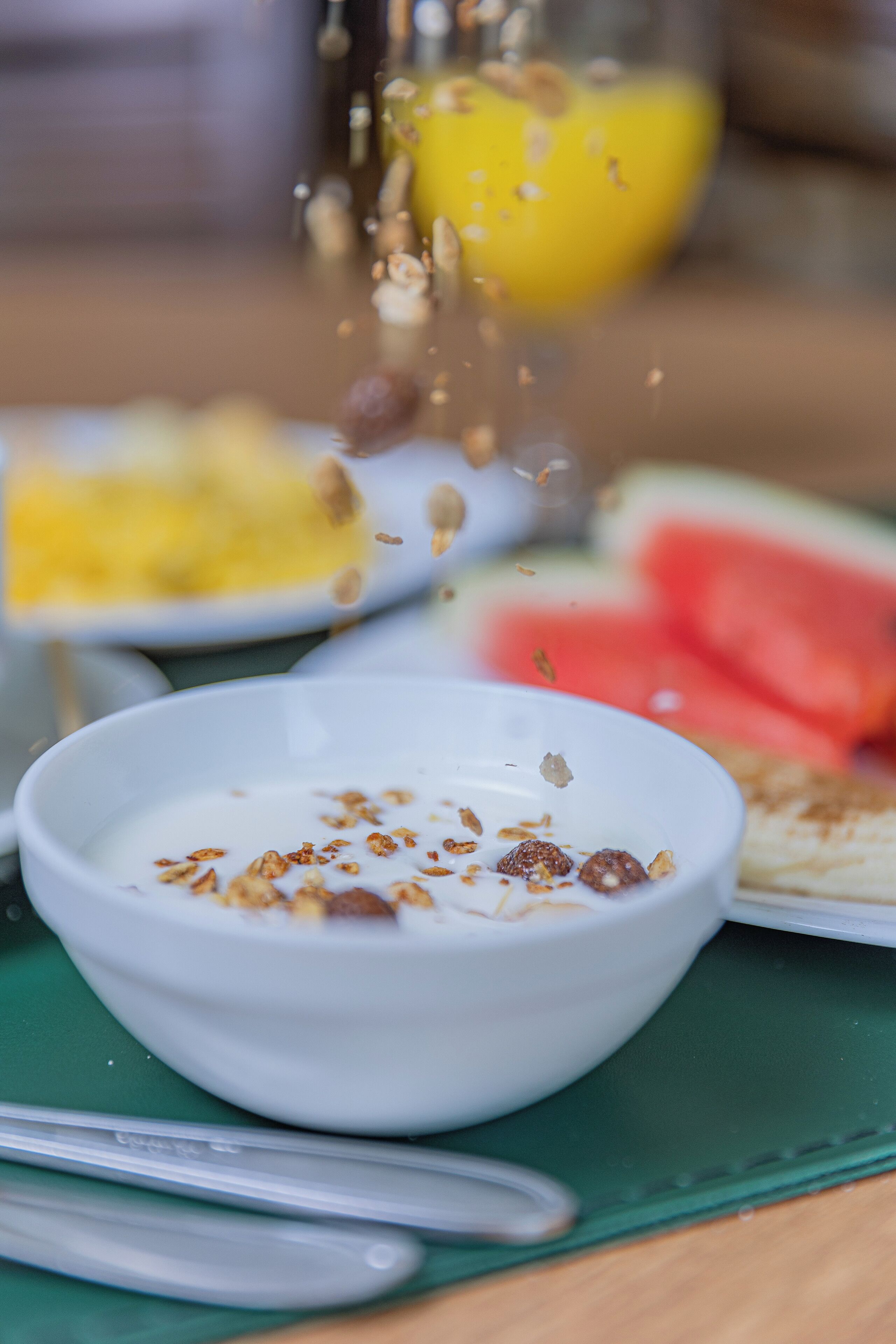 A bowl of yogurt with granola and a spoon on a green placemat.