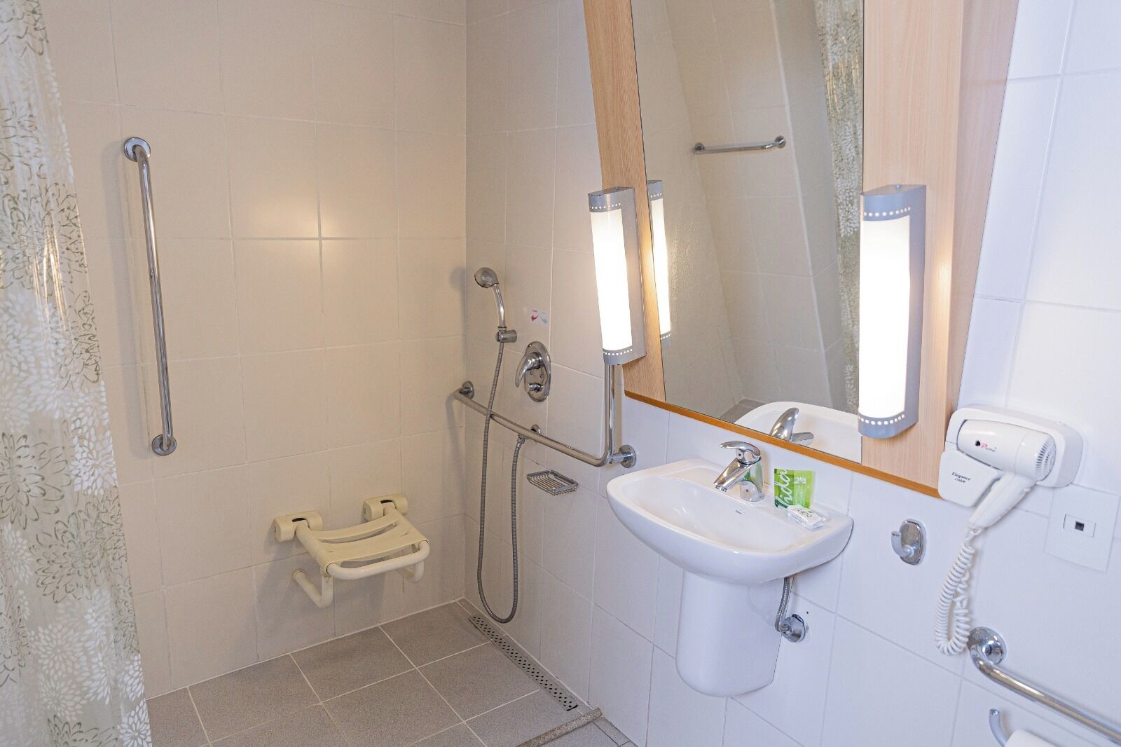 Une salle de bain équipée d’une douche, d’un lavabo, d’un miroir et d’un sèche-cheveux.