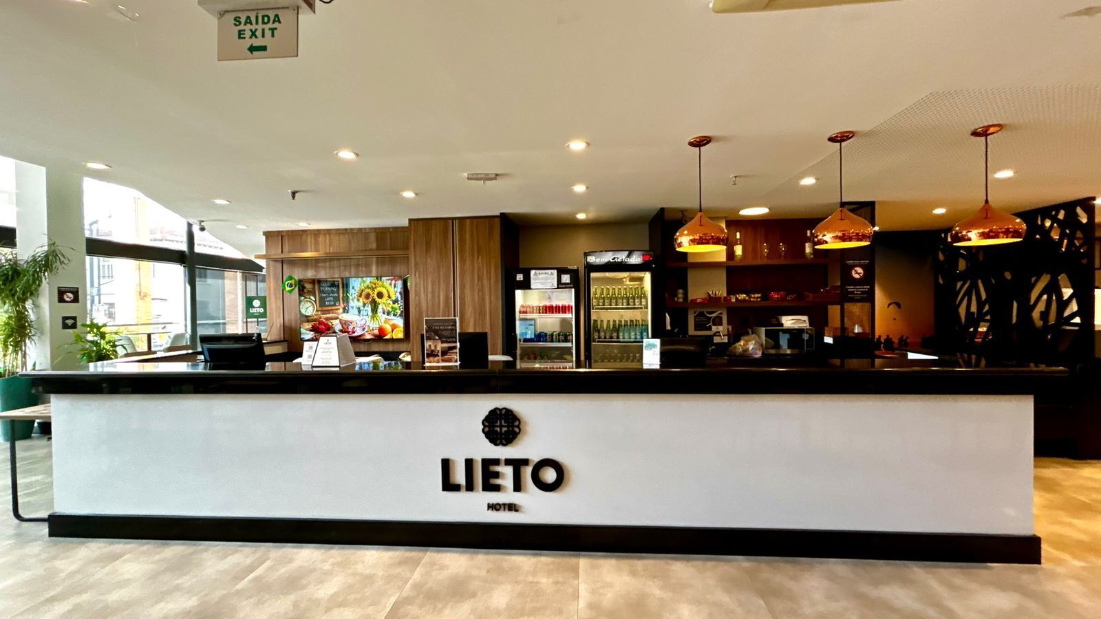 A hotel reception area with a counter, a sign indicating the exit, and a view of the outside.