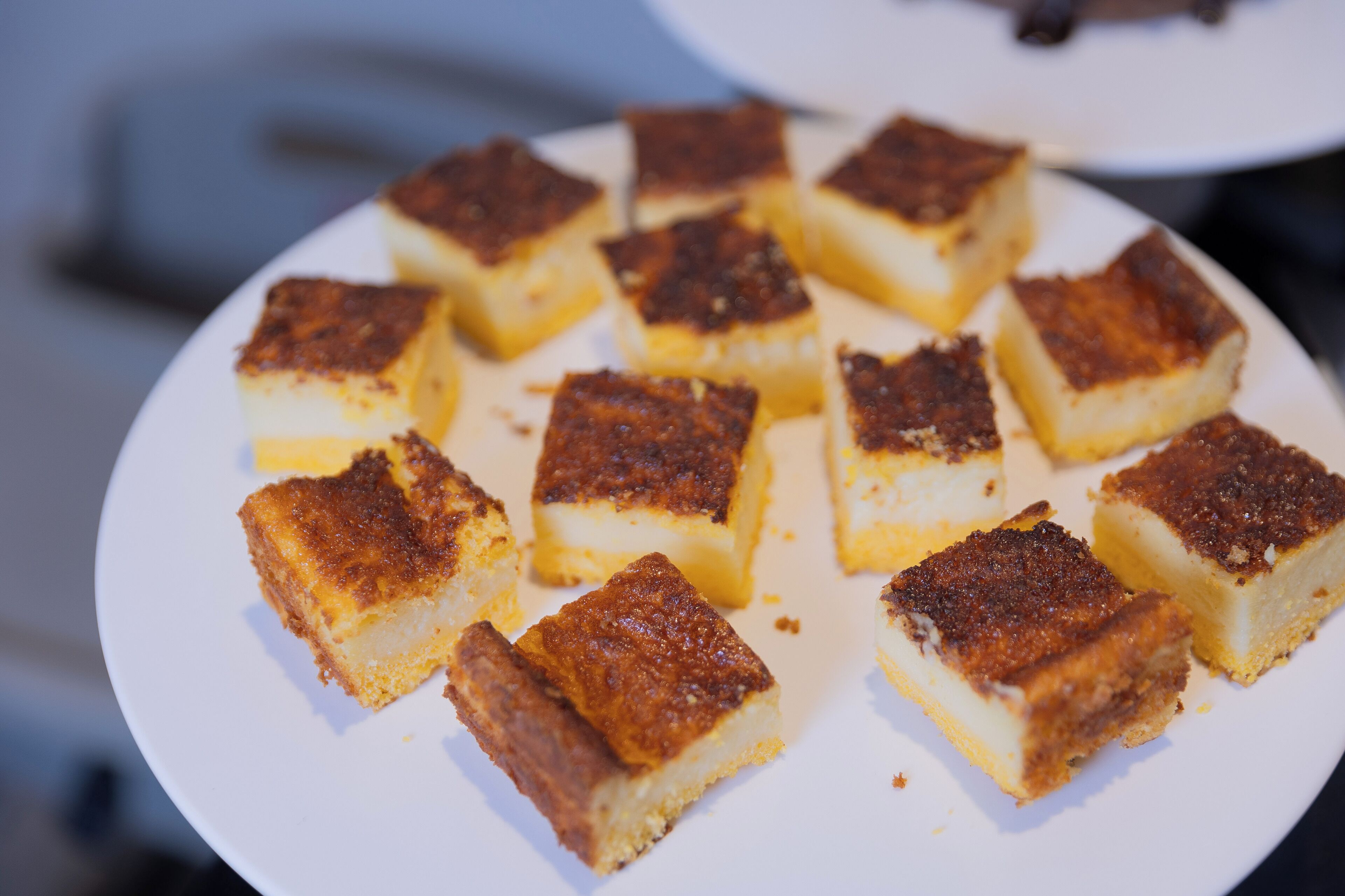 Un piatto di dolci dalla forma quadrata e dal colore marrone dorato, con una base cremosa, disposto su un piatto bianco.