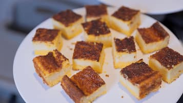 Un piatto di dolci dalla forma quadrata e dal colore marrone dorato, con una base cremosa, disposto su un piatto bianco.