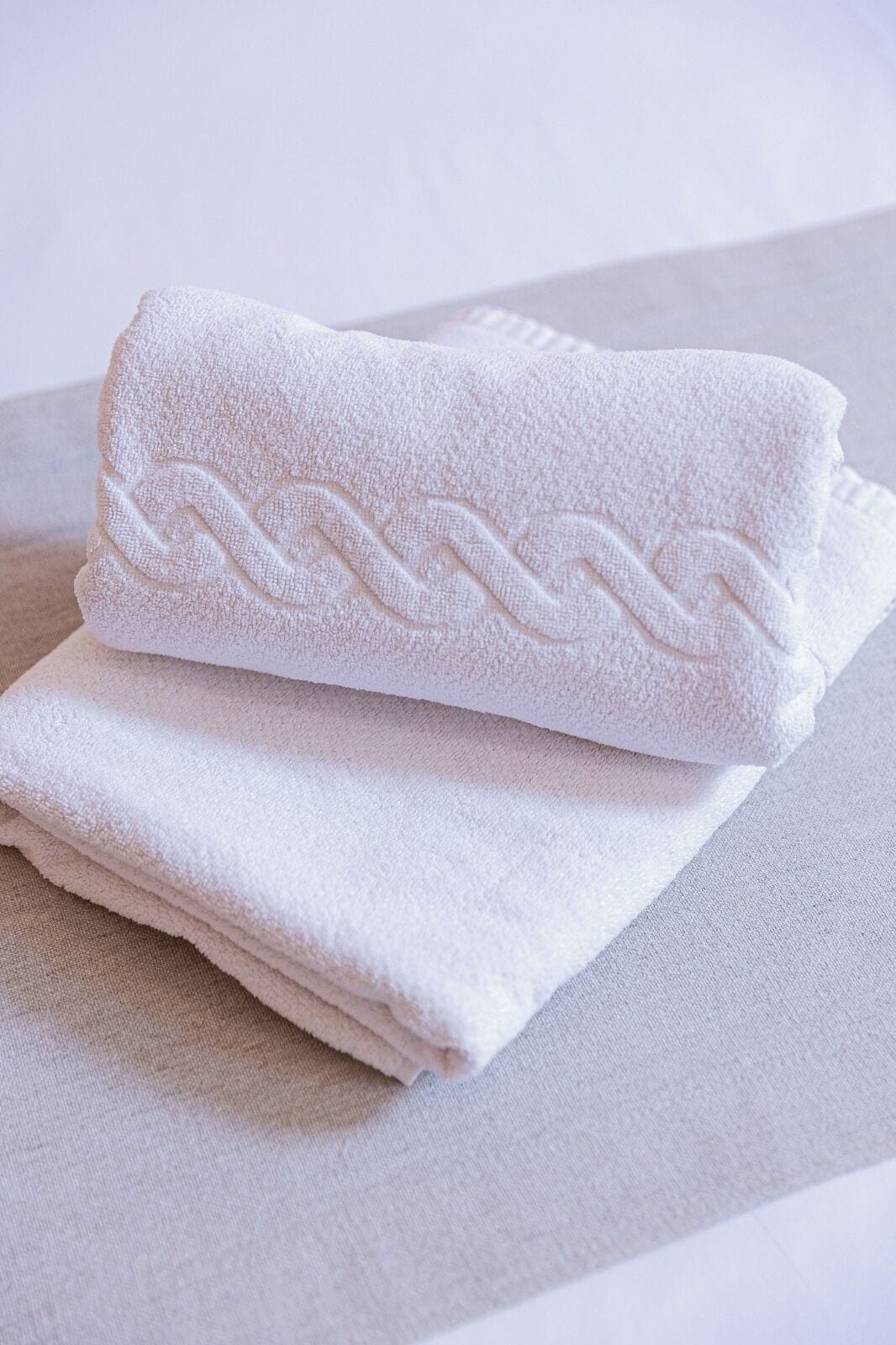 A neatly folded white towel with a textured pattern on a light-colored surface.