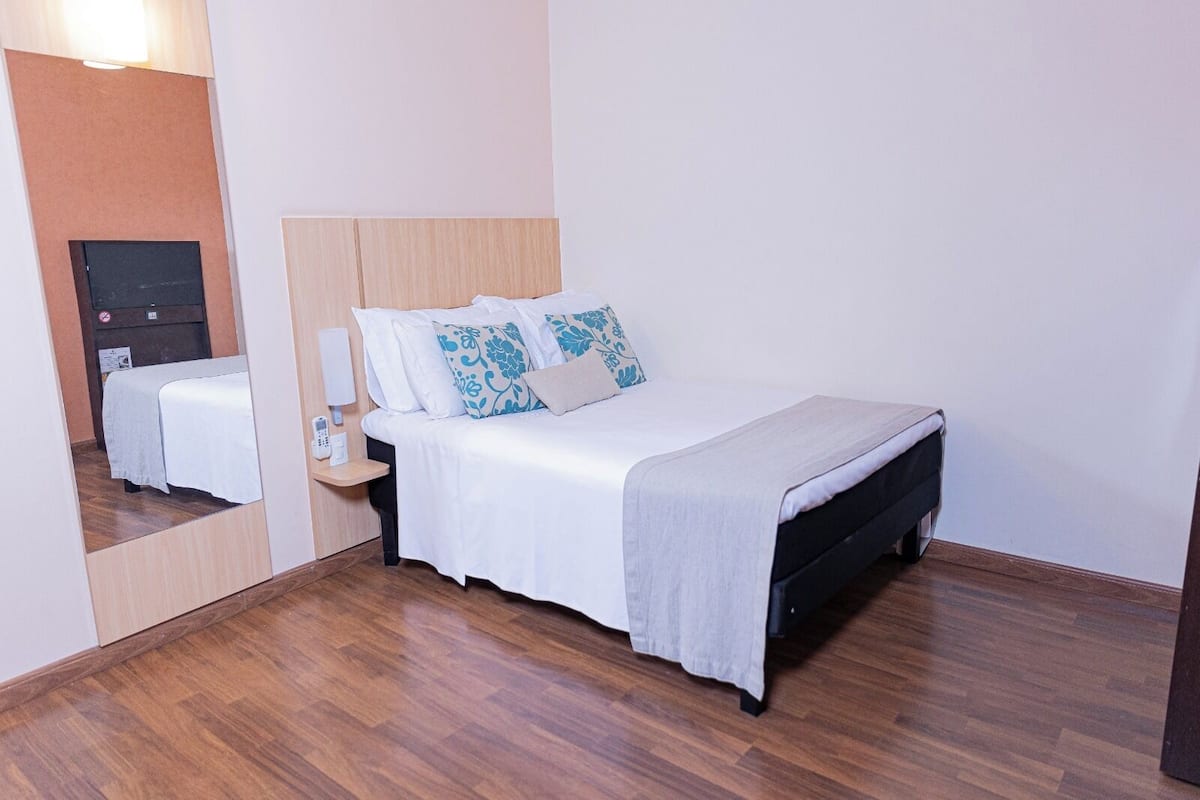 Ein ordentlich eingerichtetes Hotelzimmer mit Bett, Nachttisch und Spiegel.