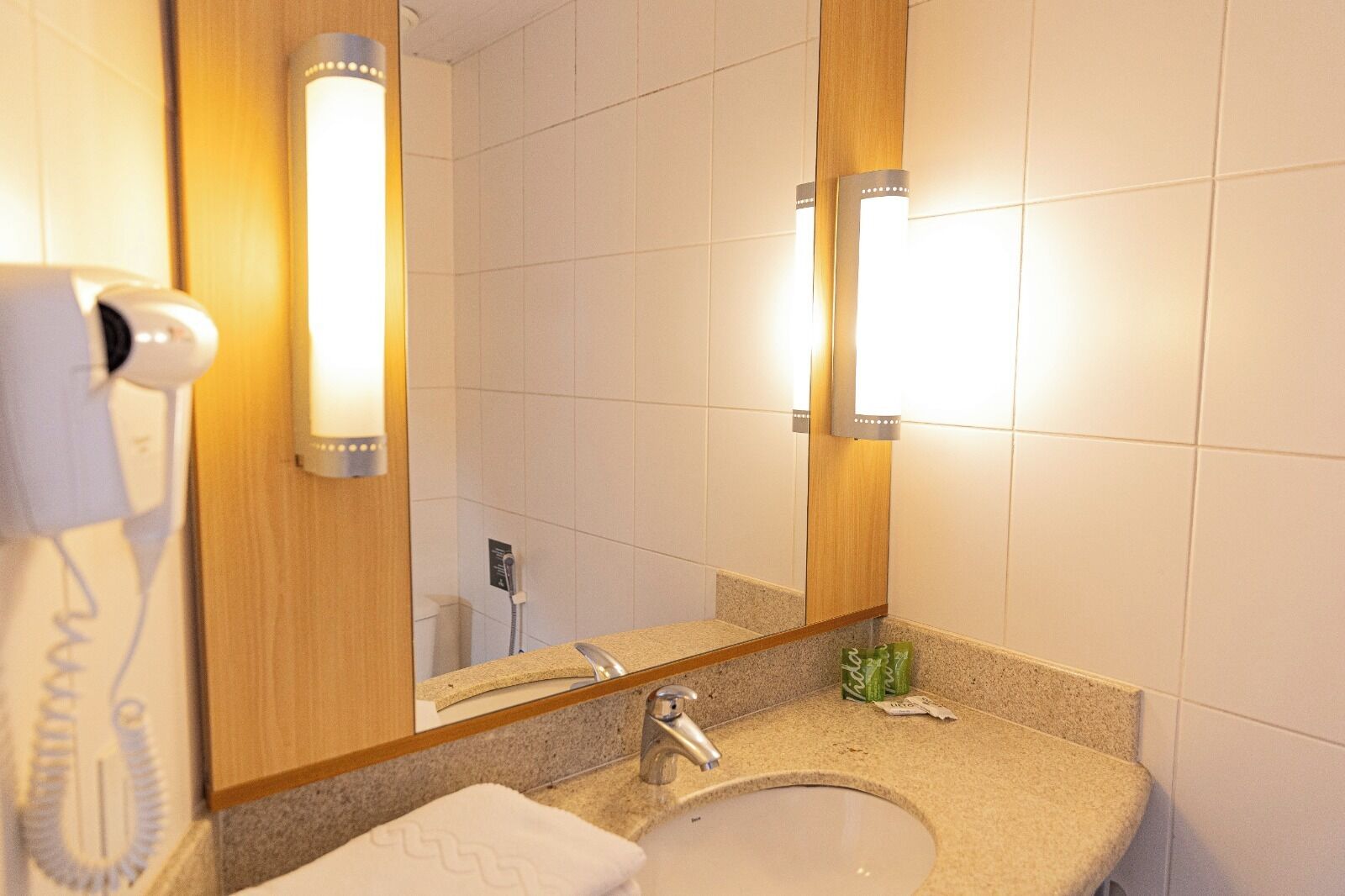 Une salle de bain d’hôtel équipée d’un lavabo, d’un miroir et d’un sèche-cheveux.