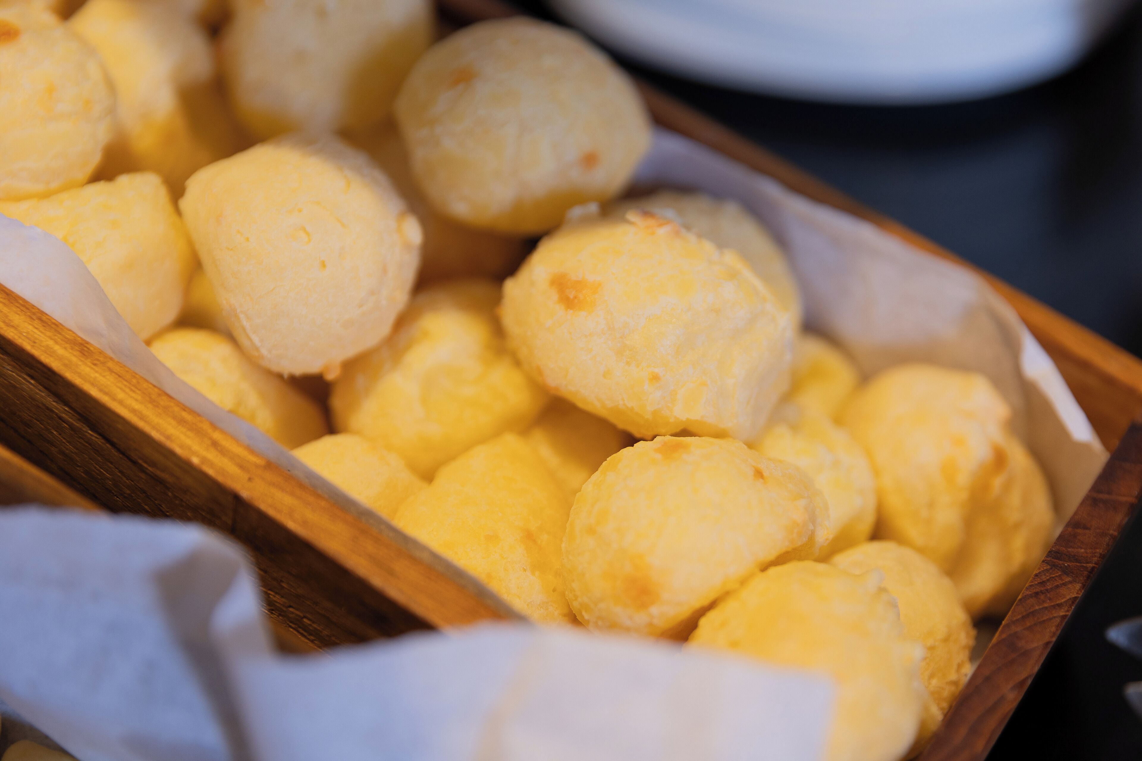 A wooden tray filled with yellow, round pastries.