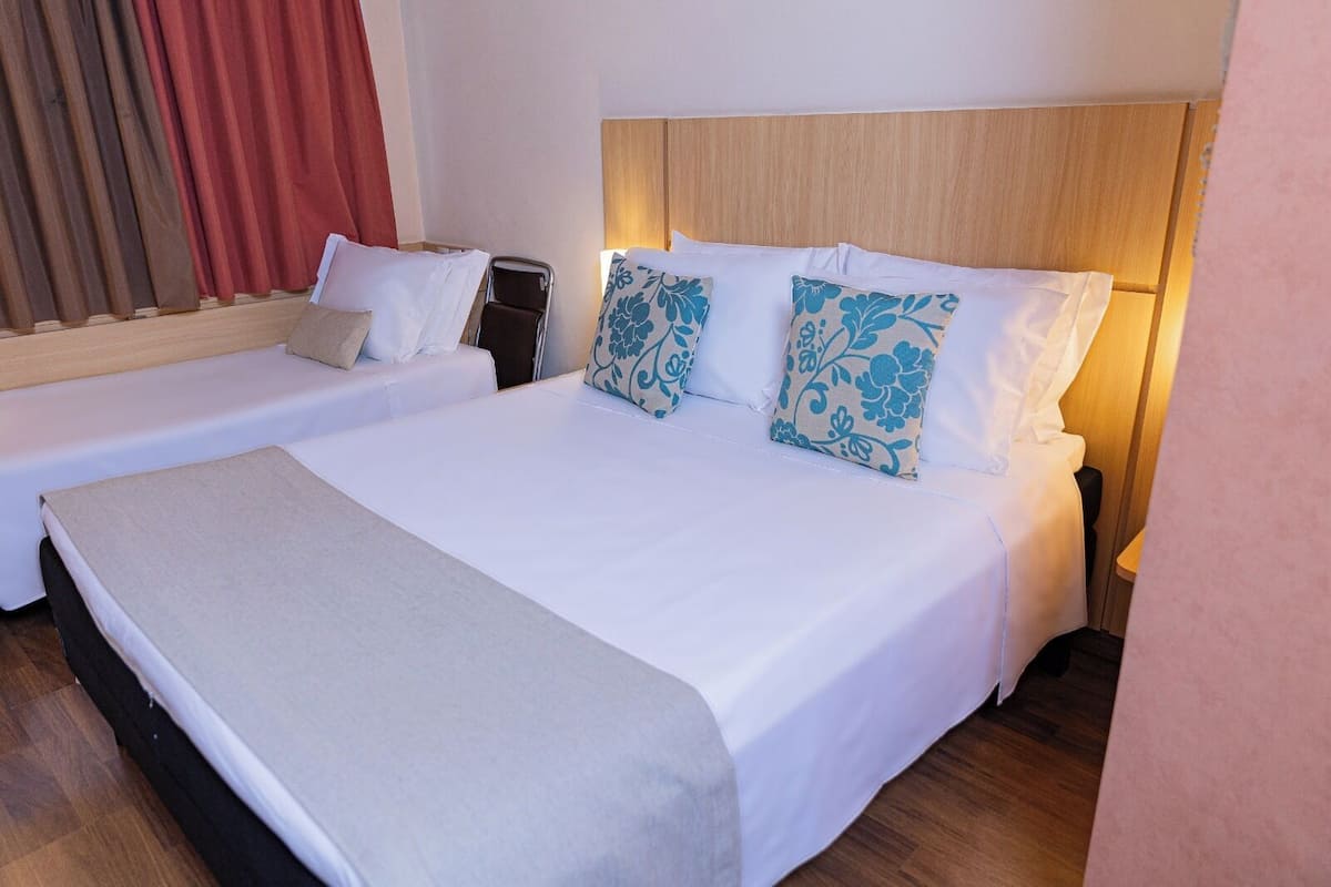 Ein Hotelzimmer mit zwei Einzelbetten, einem Holzkopfende und einem großen Bett mit Kissen mit Blumenmuster.