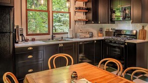 Une cuisine moderne avec des meubles de rangement aux couleurs sombres, une table à manger en bois et une fenêtre donnant sur un espace verdoyant.