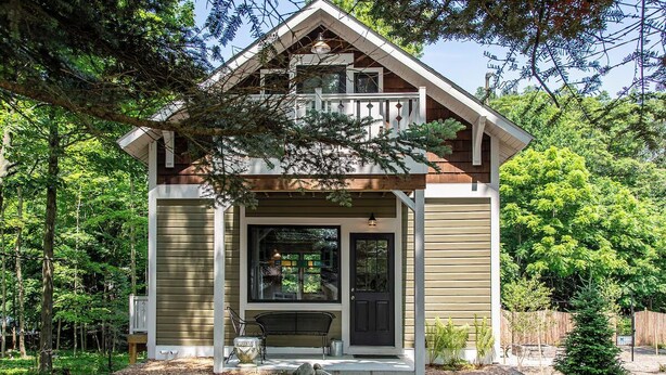 Une maison à deux étages avec un porche, un banc et un petit arbre dans le jardin.