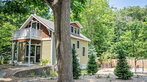 Une maison à deux étages avec un balcon, entourée d’arbres et agrémentée d’un jardin aménagé.