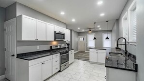 A modern kitchen with white cabinets, a black countertop, and a built-in microwave. - Comfort Zone (Wilmington)