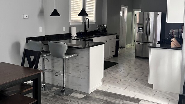 A modern kitchen with a central island, bar stools, a dining table, and a refrigerator. - Comfort Zone (Wilmington)