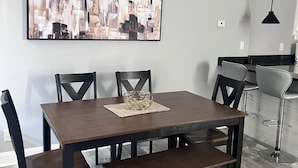 A dining area with a rectangular table, six chairs, and a bench. A cityscape painting is on the wall above the table. - Comfort Zone (Wilmington)