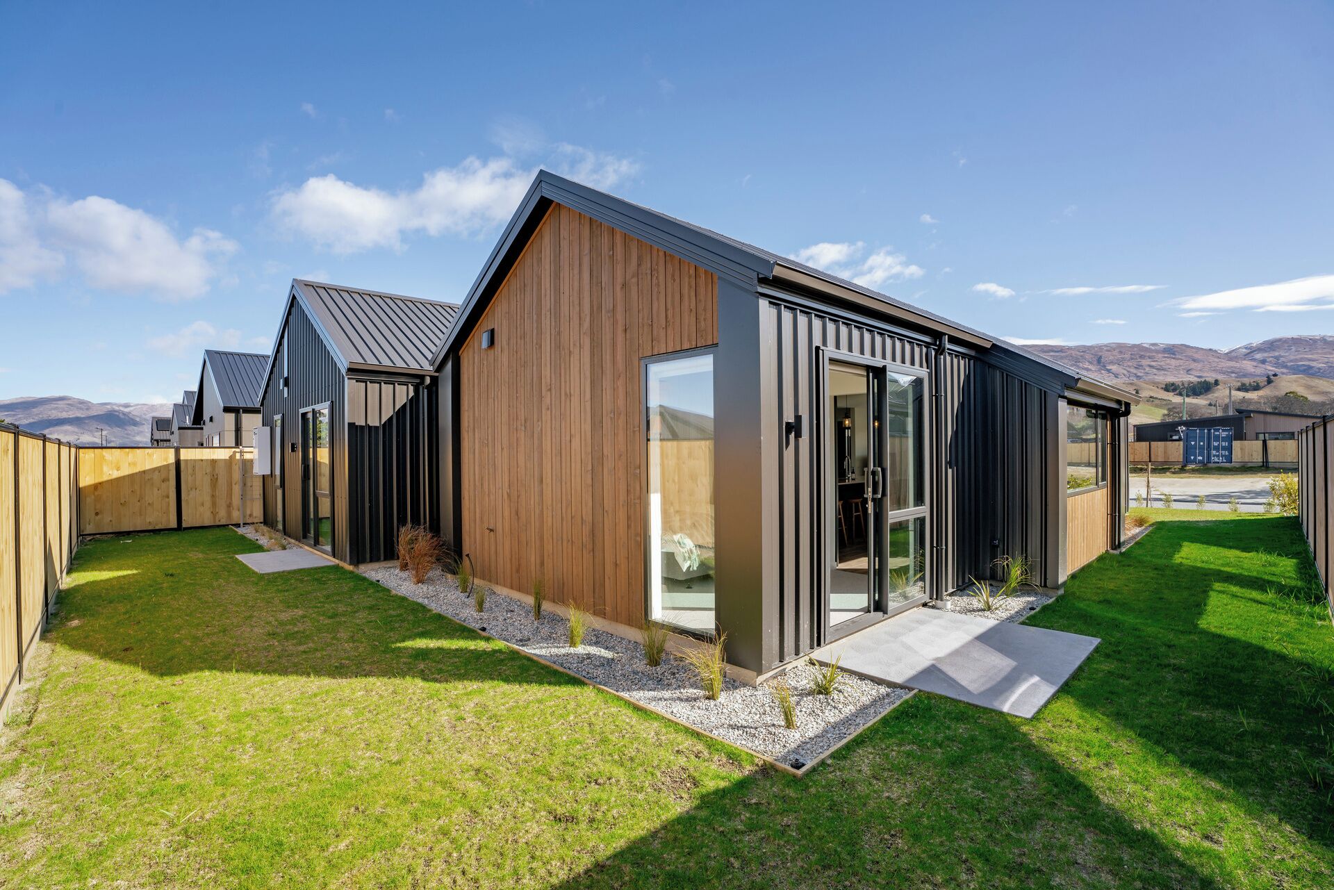 A modern house with a large glass door, a wooden exterior, and a well-maintained lawn.