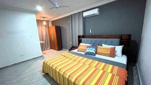 A hotel room with a large bed, a ceiling fan, an air conditioning unit, and a wardrobe. - Delightful apartment with AC in Greater Accra Region (Greater Accra Region)