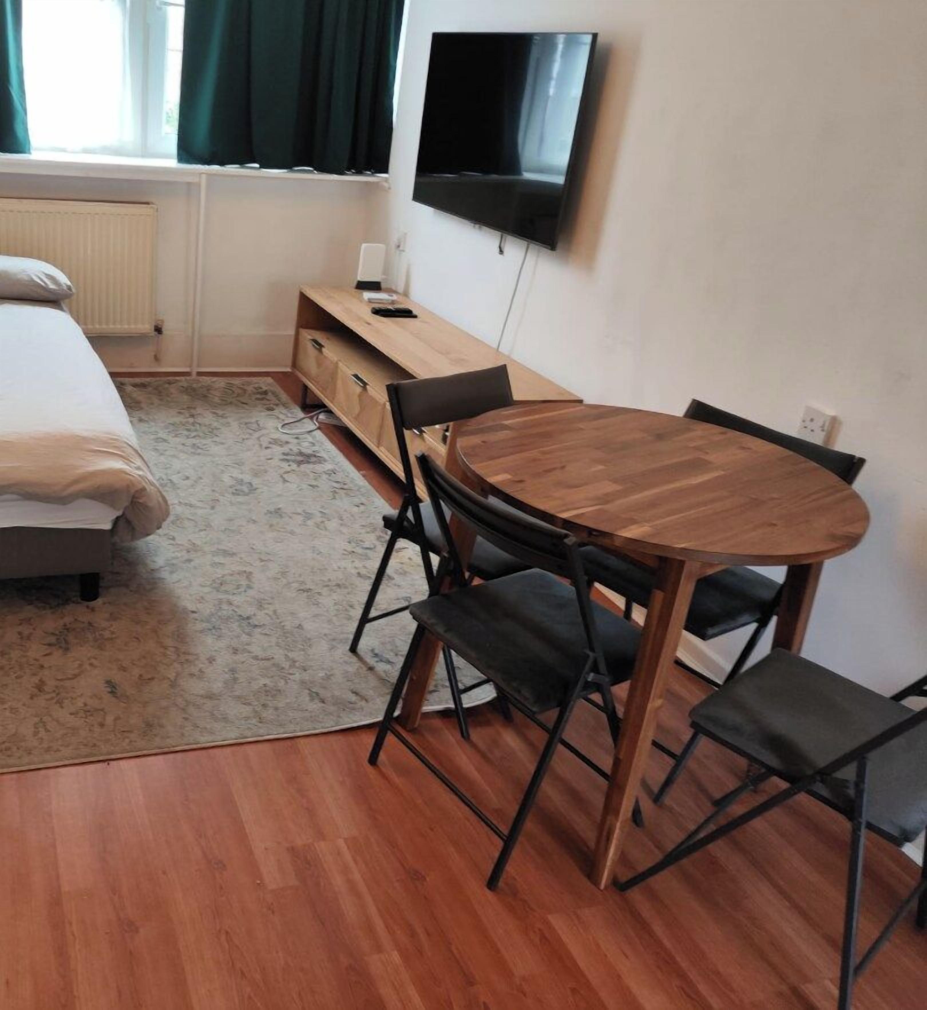 A room with a bed, a TV mounted on the wall, a wooden table with chairs, and a radiator.