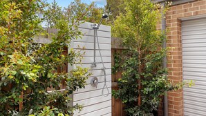 Une clôture en bois avec un portail en métal, entourée d’une végétation luxuriante et d’un mur de briques.