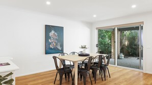 Un coin repas avec une table en bois et des chaises noires, une grande peinture abstraite au mur et une porte-fenêtre coulissante donnant sur un espace extérieur.