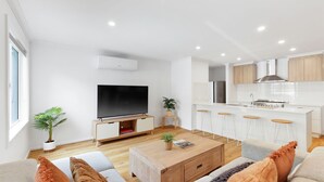 Un salon moderne avec un téléviseur à écran plat, une table basse en bois et un canapé. Il y a également un coin cuisine avec des meubles blancs et une hotte de cuisinière en acier inoxydable.