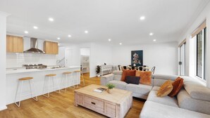 Une cuisine moderne avec des armoires blanches, une hotte de cuisinière en acier inoxydable et un coin bar avec des tabourets.