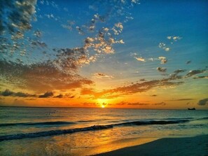 Atardecer sobre una playa con olas y un barco a lo lejos.