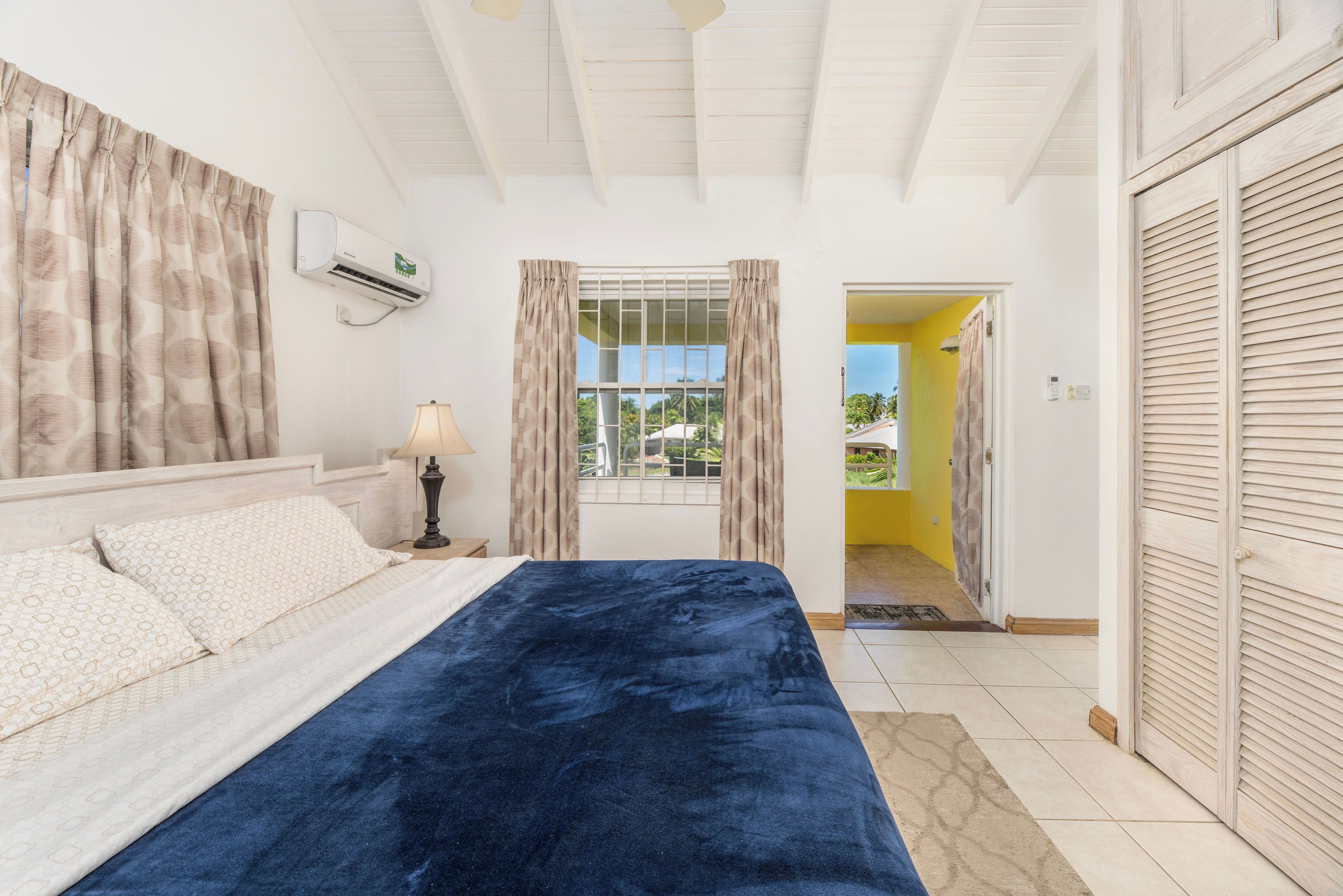 A bedroom with a bed, curtains, an air conditioning unit, and a view through a window.